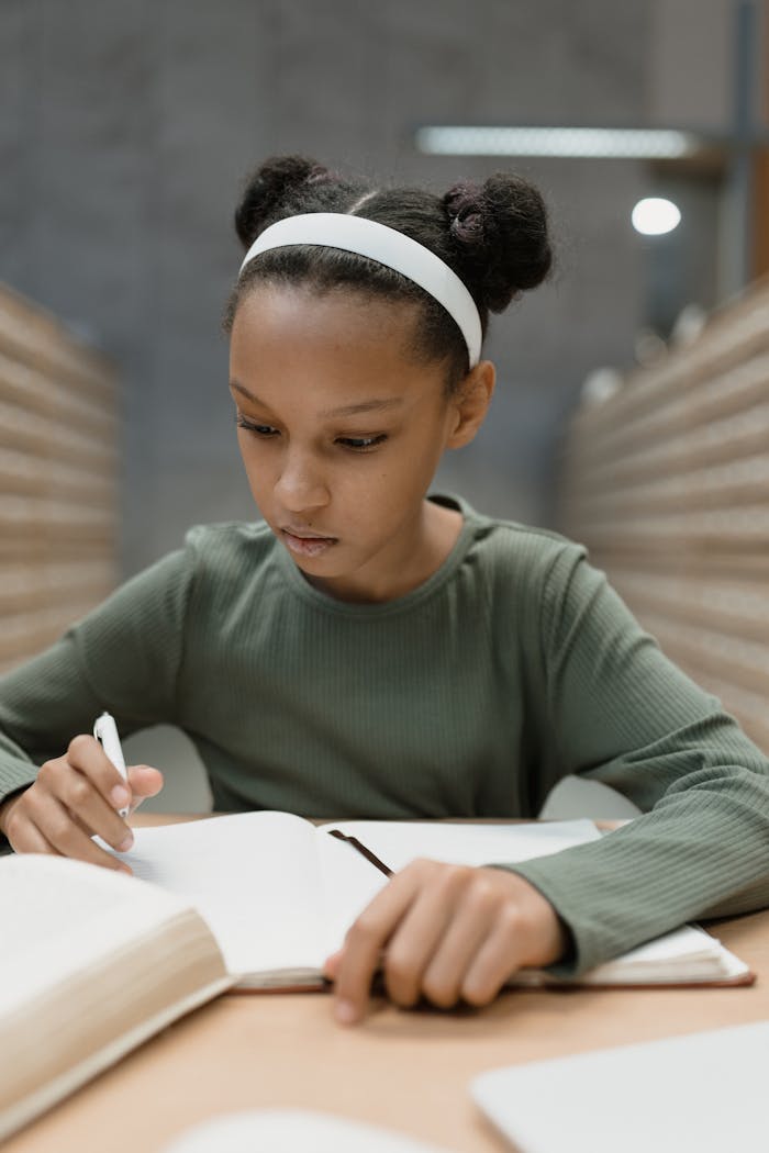 Young girl deeply focused on studying with books indoors at a library setting.