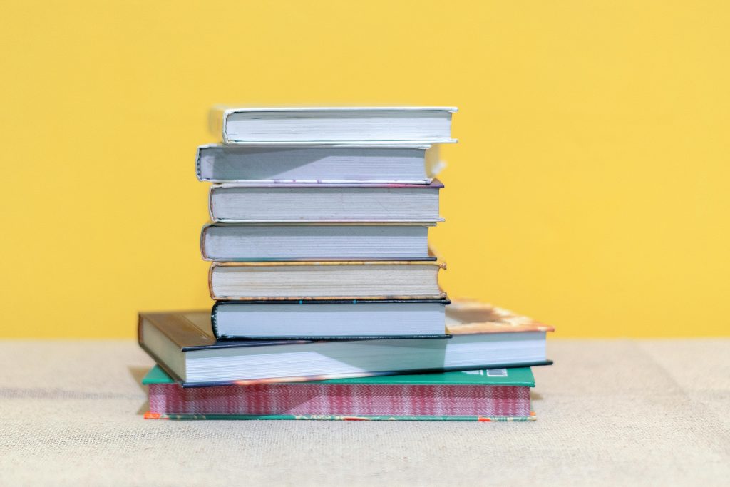 A stack of various books against a bright yellow background, ideal for education themes.